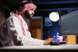 Muslim man types code on a desktop PC. He excels in app programming and showcases his expertise in software development and algorithms. This image represents the evolving world of digital technology. photo