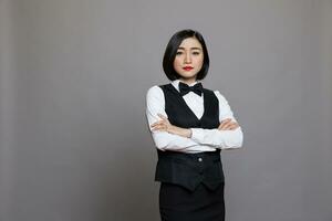 Professional asian woman waitress standing with arms crossed portrait. Serious receptionist in uniform showing confidence while posing with folded hands and looking at camera photo