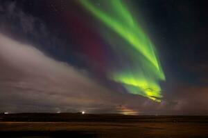 Aurora borealis terminado nieve cubierto ladera en invernal alrededores. islandés del Norte luces son magnífico espectáculo de naturaleza, brillante el Noche cielo en un glacial paisaje. foto