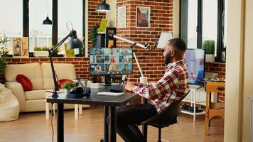 Cheerful employee in video conference meeting chatting with diverse international team while working from home. Man teleworking in online video call with coworkers remotely from cozy apartment photo