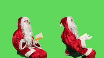 Saint nick reads poetry book in studio against isolated greenscreen backdrop, enjoying lecture of fairytale fiction or novel. Wise man reading literature for education, santa claus character. photo