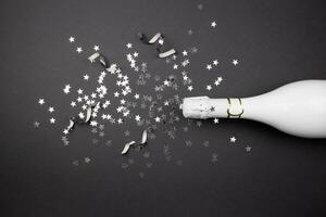 Champagne bottle and confetti on dark background. Flat lay composition of celebration. Top view. photo