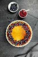 Delicious cheesecake tart with fresh blueberries and cranberries on a dark stone background. Top view. photo