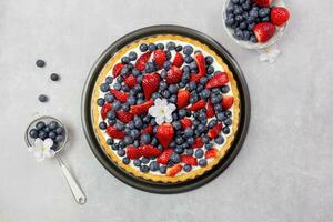 Delicious blueberry and strawberry tart with whipped cream and mascarpone on a light gray concrete background. Top view. photo