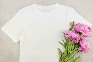 White womens cotton t-shirt mockup with pink peony flowers on gray concrete background. Design t shirt template, print presentation mock up. Top view flat lay. photo