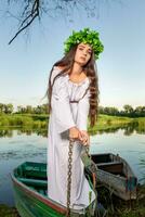 Young woman with flower wreath on her head, relaxing on boat on river at sunset. Concept of female beauty, rest in the village photo