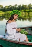 el ninfa con largo oscuro pelo en un blanco Clásico vestir sentado en un barco en el medio de el río. foto