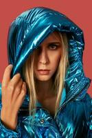 Blonde slim girl in blue down jacket covers her face from wind with hood photo