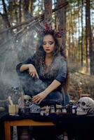 Witch in black, long dress, with red crown in her long hair. Posing in pine forest. Making a magic potion. Spells and witchcraft. Close-up, smoke. photo