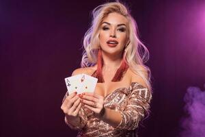 Blonde woman with a perfect hairstyle and bright make-up is posing with playing cards in her hands. Casino, poker. photo