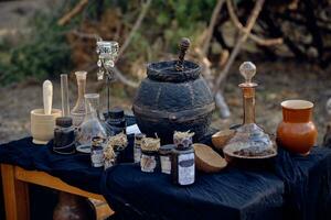 Table with accessories for spells and witchcraft standing in pine forest. Magic potion is brewed in black pot. Close-up. photo