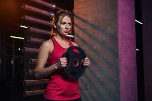 Girl athlete keeps the disc from the bar weighting agent for doing crossfit and fitness. photo