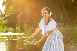 Young beautiful caucasian woman standing at the bank of river. Traditional countryside picture with girl at foreground and copy space. Sun flare photo