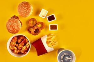 Fast food dish top view. French fries, hamburger, mayonnaise and ketchup sauces on yellow background. photo