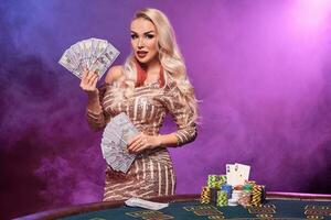 Blonde woman with a perfect hairstyle and bright make-up is posing with playing cards in her hands. Casino, poker. photo