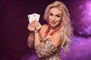 Blonde woman with a perfect hairstyle and bright make-up is posing with playing cards in her hands. Casino, poker. photo