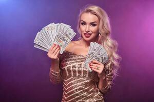 rubia mujer con un Perfecto peinado y brillante maquillaje es posando con ventilador de cien dólar cuentas en su manos. casino, póker. foto