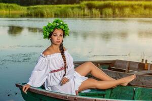 Young sexy woman on boat at sunset. The girl has a flower wreath on her head, relaxing and sailing on river. Fantasy art photography. photo