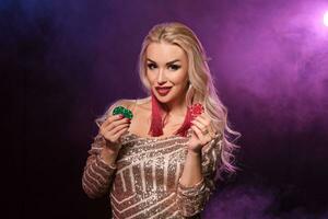 Blonde woman with a perfect hairstyle and bright make-up is posing with gambling chips in her hands. Casino, poker. photo