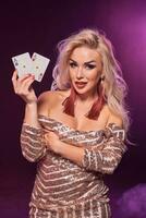 rubia mujer con un Perfecto peinado y brillante maquillaje es posando con jugando tarjetas en su manos. casino, póker. foto