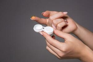 Contact eye lens. Close-up of woman hands holding white eye lense container. Woman fingers holding eye lense box. photo