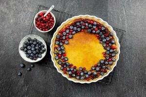 Delicious cheesecake tart with fresh blueberries and cranberries on a dark stone background. Top view. photo