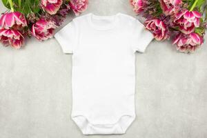 White baby girl or boy bodysuit mockup flat lay with tulip flowers on gray concrete background. Design onesie template, print presentation mock up. Top view. photo