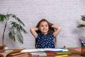 Thoughtful little girl at the table draw with crayons photo