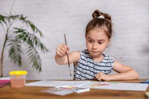 inspirado pequeño niña a el mesa dibujar con pinturas foto