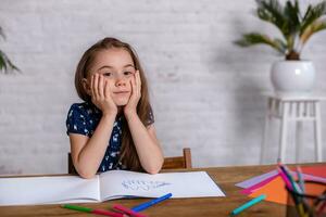 Thoughtful little girl at the table draw with crayons photo