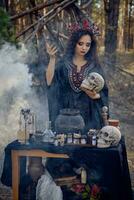 Witch in black, long dress, with red crown in her hair. Posing in pine forest, holding skull, making potion. Spells and witchcraft. Close-up, smoke. photo