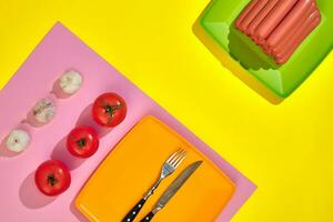 Stack of thin wiener sausages with tomatoes on plate on pink and yellow background photo