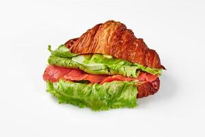 Croissant sandwich with fried egg, smoked salmon, green cheese and lettuce isolated on white photo