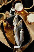 Smoked gutted bream, salted dried roach and sabrefish on wooden board with foamy light beer photo