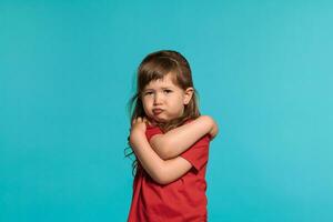 Beautiful little girl wearing in a red t-shirt is posing against a blue studio background. photo