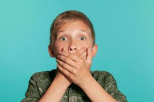 Close-up portrait of a blonde teenage boy in a green shirt with palm print posing against a blue studio background. Concept of sincere emotions. photo