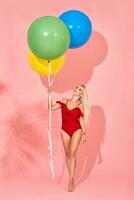 Young sexy slim woman in a red swimsuit with balloons in her hand is posing in a studio. photo