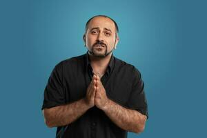 Close-up portrait of a brunet middle-aged man with beard, dressed in a black t-shirt and posing against a blue background. photo