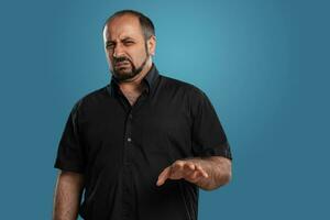 Close-up portrait of a brunet middle-aged man with beard, dressed in a black t-shirt and posing against a blue background. photo