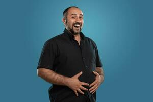 Close-up portrait of a brunet middle-aged man with beard, dressed in a black t-shirt and posing against a blue background. photo