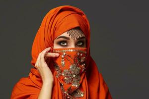 Studio shot of a young charming woman wearing the terracotta hijab decorated with sequins and jewelry. Arabic style. photo