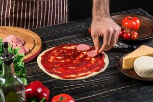 cocinar en el cocina poniendo el ingredientes en el Pizza. Pizza concepto. producción y entrega de alimento. foto