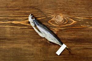 Salted dried sabrefish with paper label on tail lying on wooden surface photo