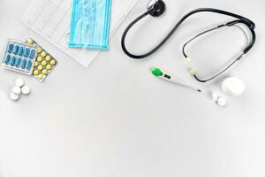 Medical equipment pills, mask, thermometer and stethoscope on white background. Top view. Copy space photo