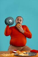 de cerca retrato de un de edad mediana hombre con barba, vestido en un rojo suéter tipo con cuello de tortuga, posando con hamburguesas y francés papas fritas azul antecedentes. rápido alimento. foto