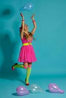 encantador niña con un multicolor trenzas peinado y brillante constituir, posando en estudio con aire globos en contra un azul antecedentes. foto