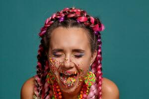 encantador niña con un multicolor trenzas peinado y brillante constituir, posando en estudio en contra un azul antecedentes. vistoso Adición es en su rostro. foto