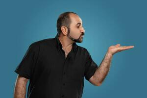 Close-up portrait of a brunet middle-aged man with beard, dressed in a black t-shirt and posing against a blue background. photo