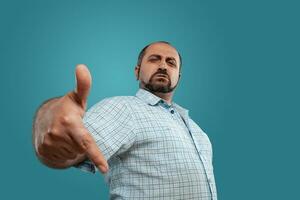 Close-up portrait of a brunet middle-aged man with beard, dressed in a light checkered shirt and posing against a blue background. photo