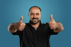 Close-up portrait of a brunet middle-aged man with beard, dressed in a black t-shirt and posing against a blue background. photo